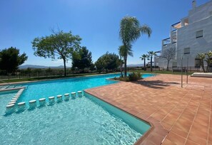 Una piscina con acqua cristallina e azzurra, circondata da una terrazza piastrellata e palme.