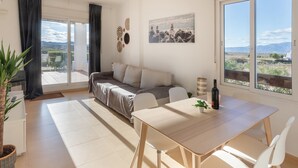 Een moderne woonkamer met een bank, een eettafel, stoelen, grote ramen met uitzicht en een potplant.