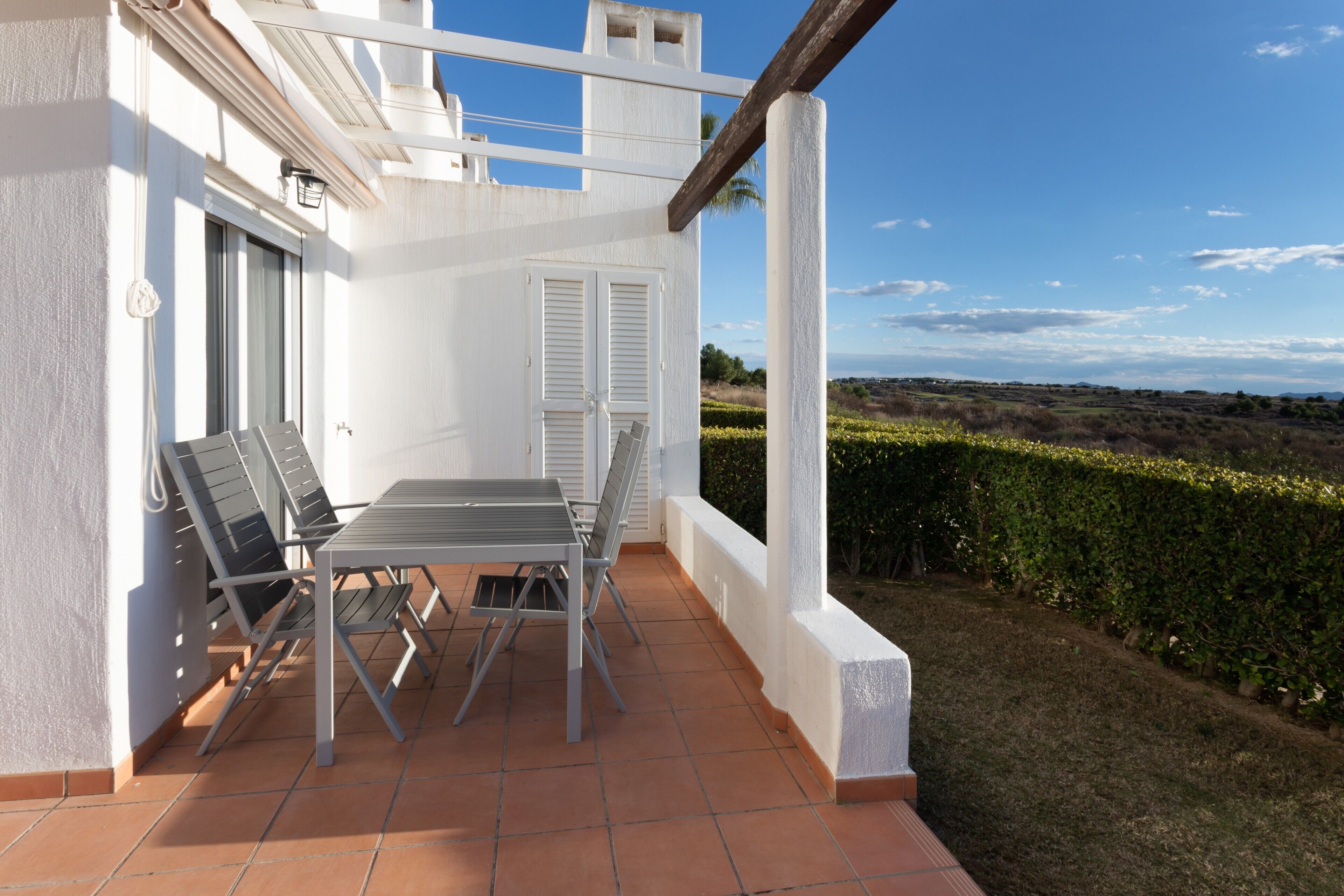 A terrace with a table and chairs, a door, and a view of the landscape.