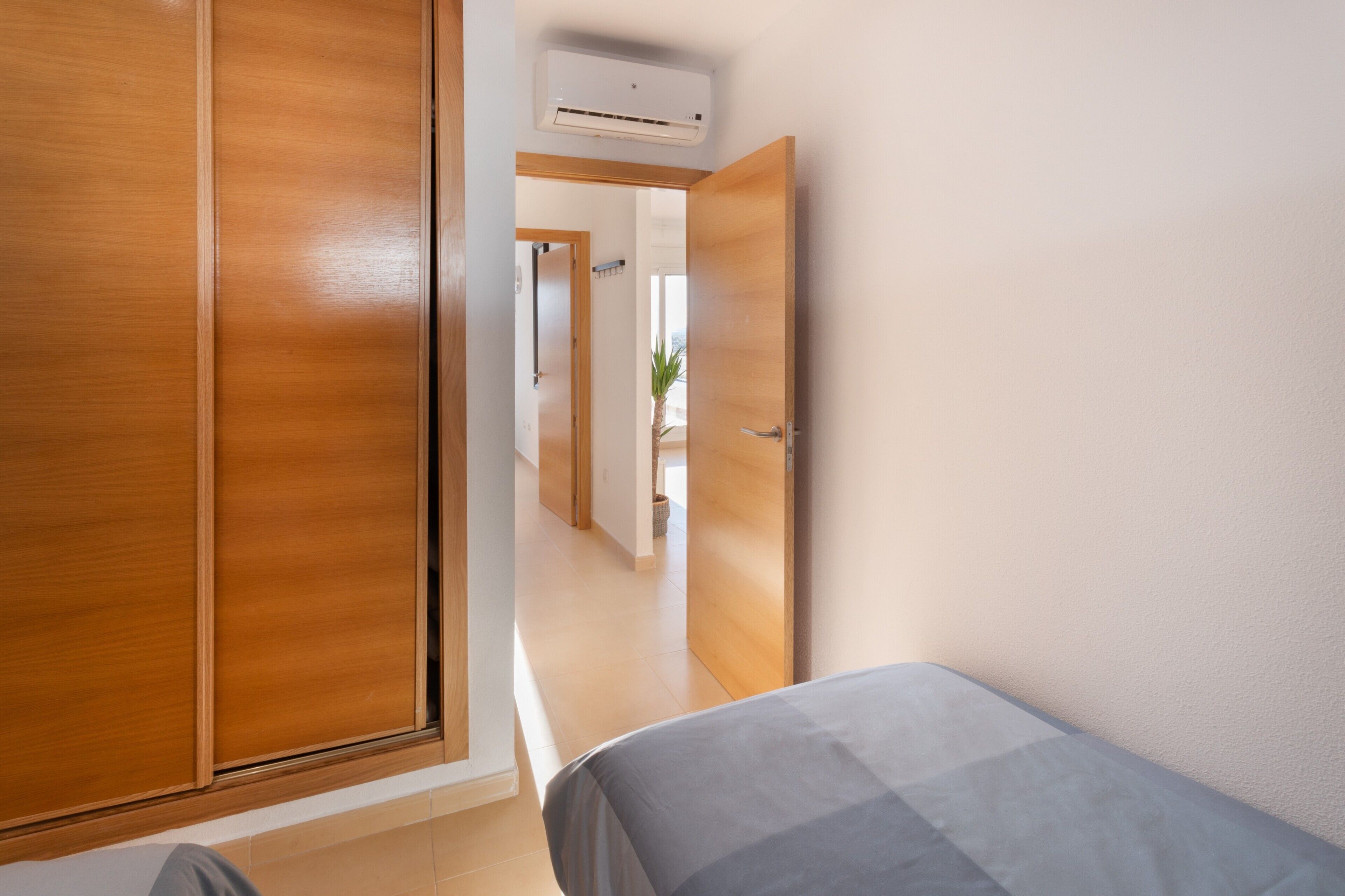 A bedroom with a bed, wooden wardrobe, and an air conditioning unit.
