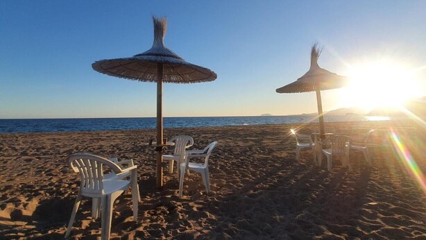 Een strand met rieten parasols en witte plastic stoelen.