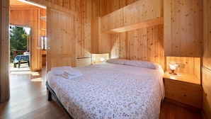 Ein Zimmer aus Holz mit einem Bett, einem Nachttisch und einer Tür, die nach draußen führt.