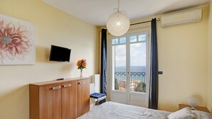 Ein Schlafzimmer mit einem Bett, einem Fernseher, einem Fenster mit Vorhängen, einer Heizung und einem an der Wand hängenden Kunstwerk.