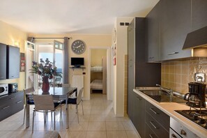 A compact kitchen with a dining area, a clock on the wall, and a small TV.