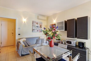 Un espacio habitable pequeño con kitchenette, un sofá, una mesa de comedor y un jarrón decorativo.