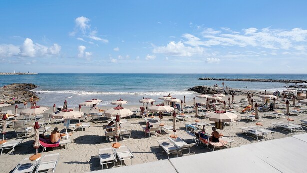 A beach with rows of sun loungers and umbrellas, a rocky shoreline, and calm sea. - Apartment "Raineri" with Sea View, Wi-Fi, A/C and Balcony (IMPERIA)