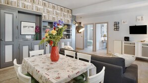 A dining area with a table set for four, a bookshelf, a television, and a sofa in the background. - Apartment "Raineri" with Sea View, Wi-Fi, A/C and Balcony (IMPERIA)