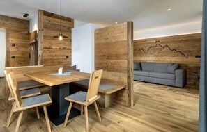 Un intérieur moderne avec une table à manger en bois, des chaises, un canapé et un luminaire fixé au mur.