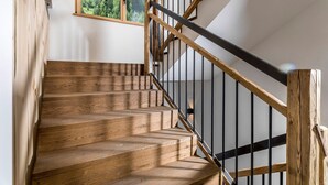 A wooden staircase with a black metal railing, a window with a forest view, and a white wall. - Apartment "Waidacherhof Alm" with Mountain View, Balcony & Wi-Fi (Prags)