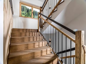 Un escalier en bois avec une rampe en métal noir, une fenêtre donnant sur la forêt et un mur blanc.