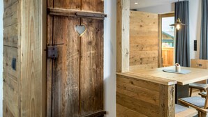 A wooden door with a heart-shaped cutout, a wooden bench, and a table with chairs in a room with wooden walls and a hanging light fixture. - Apartment "Waidacherhof Alm" with Mountain View, Balcony & Wi-Fi (Prags)