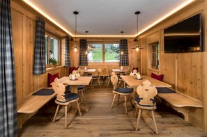 A restaurant with wooden walls, plaid curtains, and a central table with chairs.