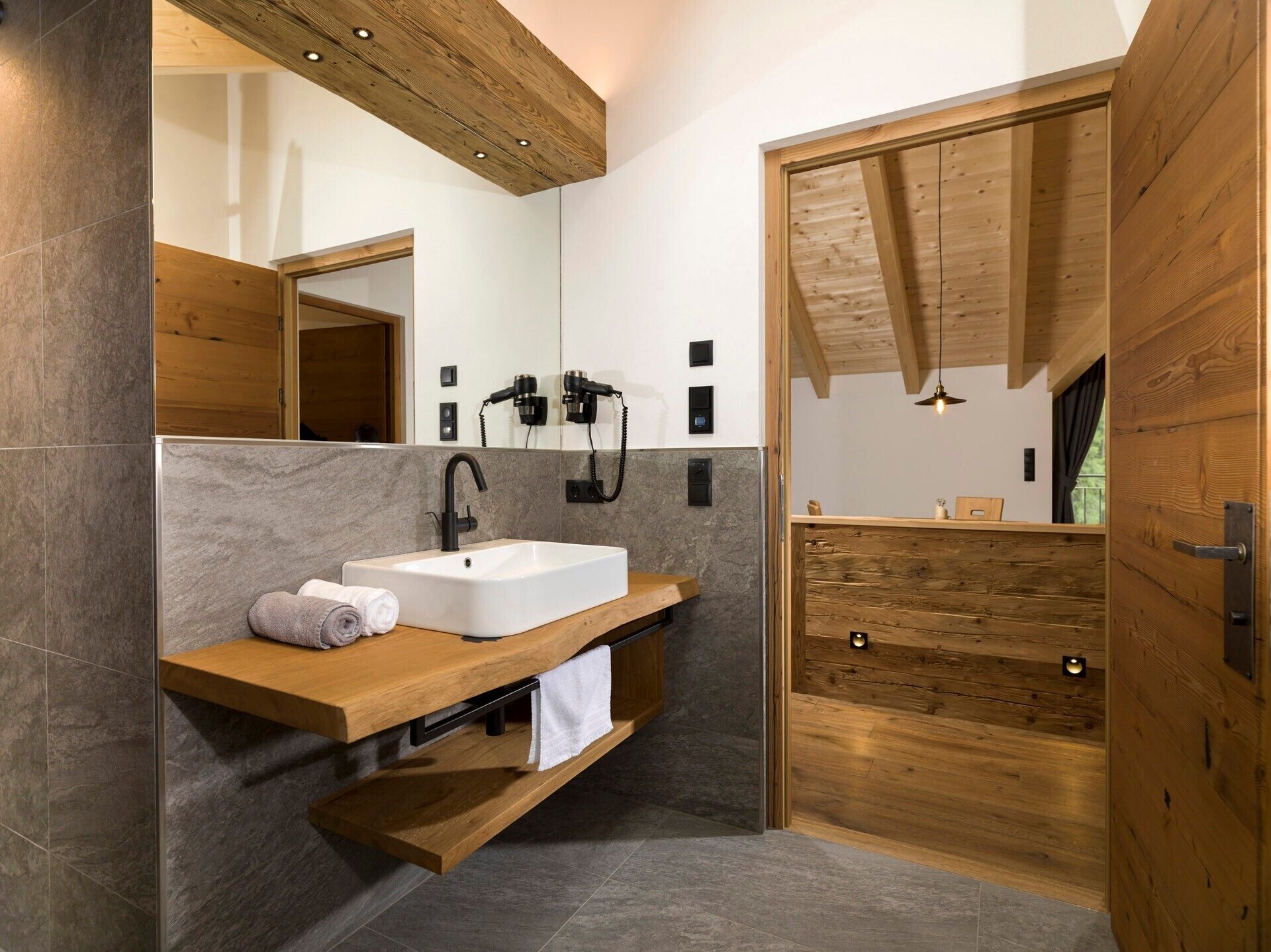 A modern bathroom with a wooden vanity, a large mirror, and a shower area.