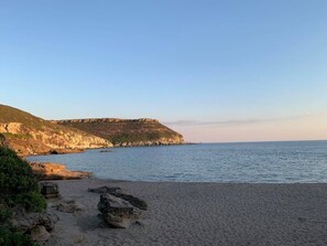 Una playa con costa rocosa, un acantilado y mar tranquilo.