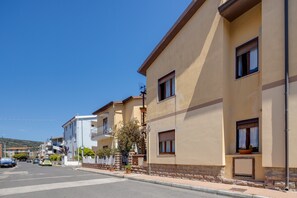 A residential street with multi-story buildings, a clear sky, and parked cars.