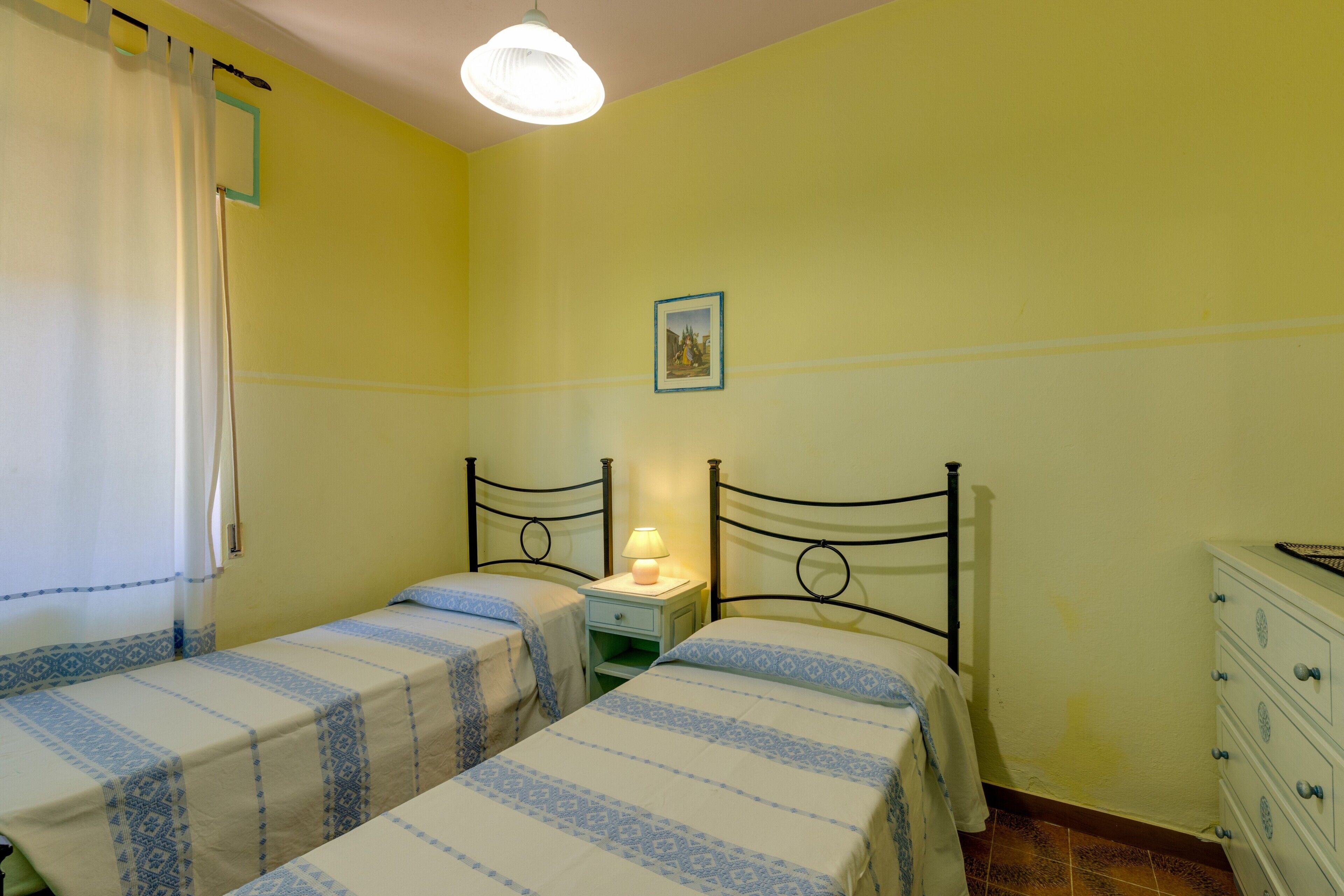 A room with two single beds, a nightstand with a lamp, a dresser, and a framed picture on the wall.