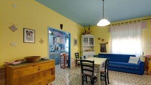 Een zithoek met een tafel en stoelen, een blauwe bank en een keuken op de achtergrond.