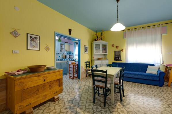 Un comedor con una mesa y sillas, un sofá azul y una cocina al fondo.