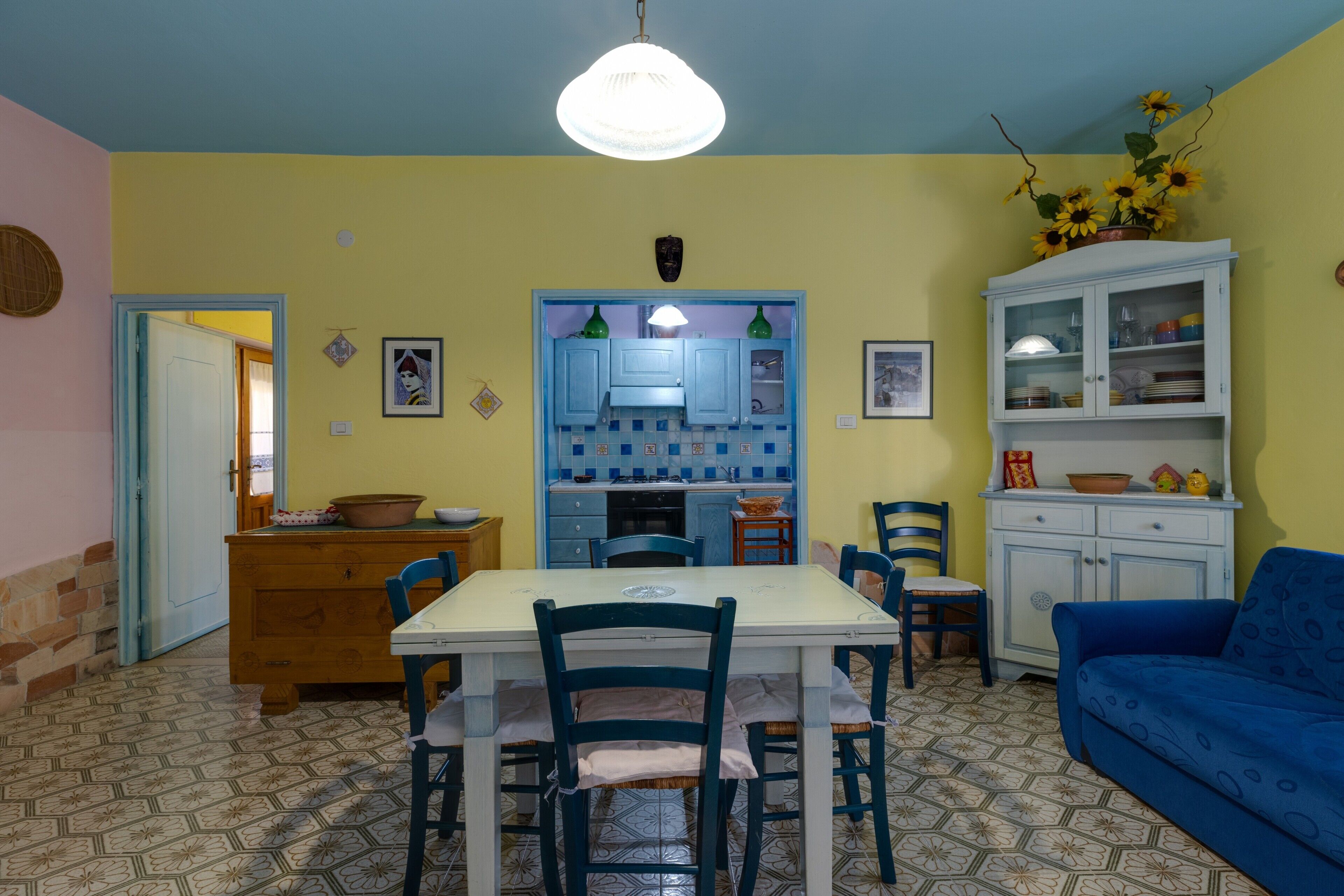 Ein Essbereich mit Tisch und Stühlen, eine Küche mit blauen Schränken und ein blaues Sofa.