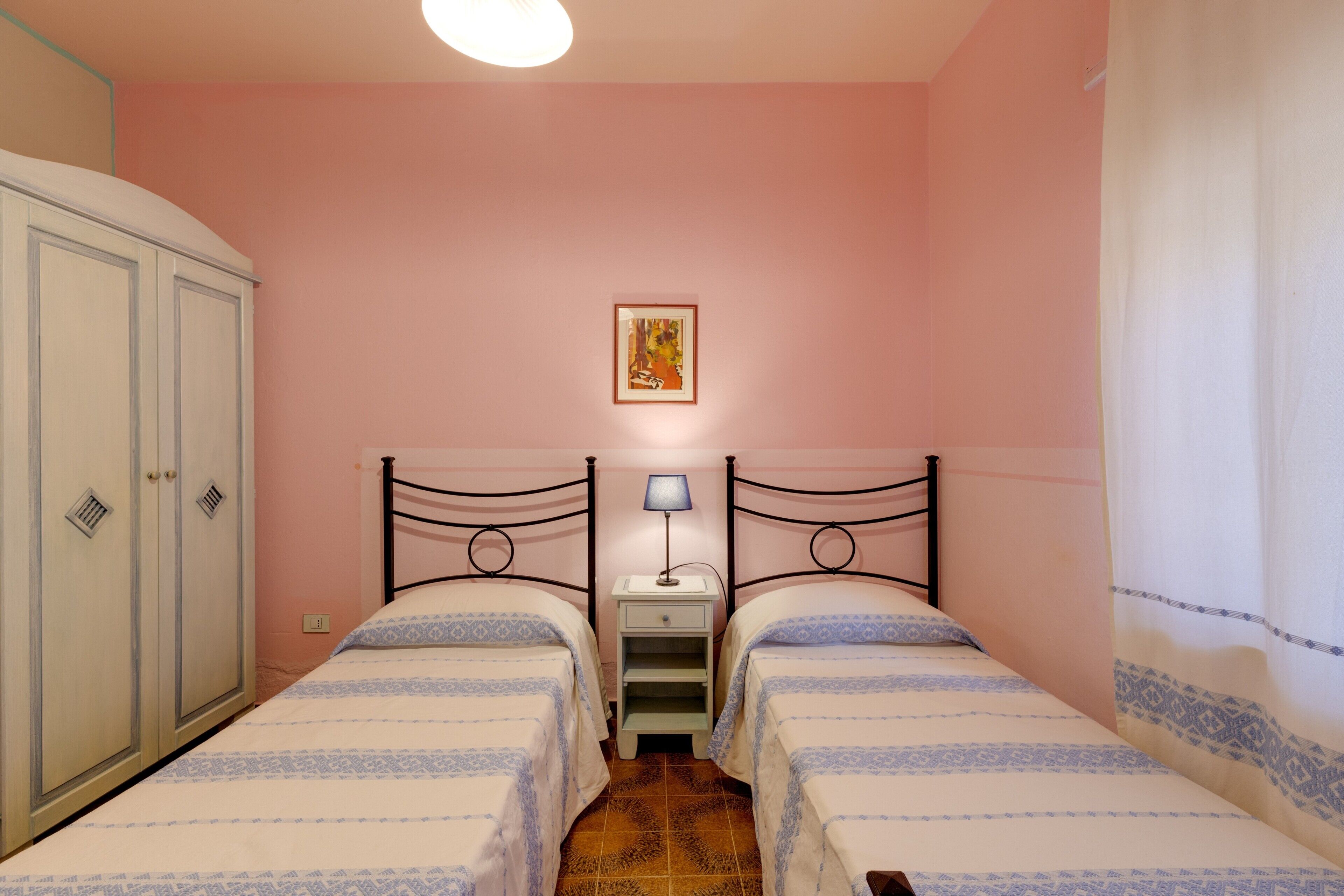 Una camera da letto con due letti, un armadio, un comodino con una lampada e un quadro appeso al muro.