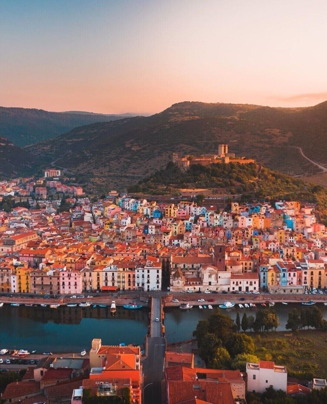 A coastal town with colorful buildings, a prominent hilltop structure, and a river.