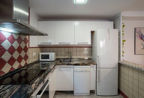 Una cocina compacta con gabinetes blancos, microondas, lavavajillas y refrigerador.