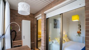 Habitació d'hotel amb una cadira de fusta, una porta blanca i una porta corredissa de vidre a un balcó, i un llit amb almoinades grogues.