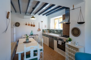 Une cuisine équipée d’une table à manger, de chaises, d’un évier, d’une cuisinière et de casseroles suspendues.