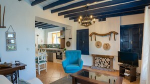 Una sala de estar con un sofá, un sillón azul, una mesa de centro de madera, un televisor y una chimenea.