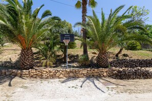 Un terrain de basket avec un panneau indicateur, entouré de palmiers et d’un mur de pierre.