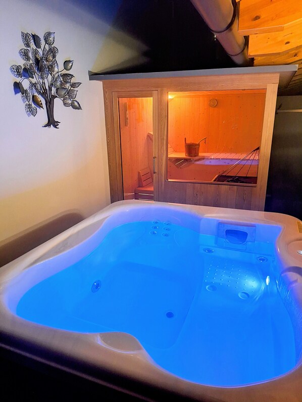 A hot tub with a blue light, wooden cabin-like structure with a sauna visible, and a wall decoration of a tree.