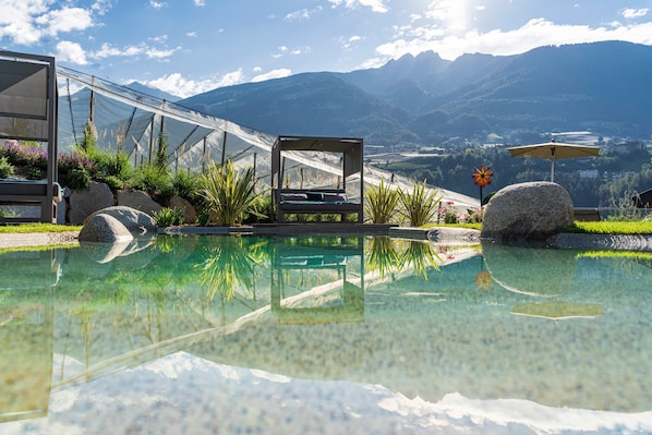 Una piscina de aguas cristalinas, rodeada de rocas y plantas, con vistas a montañas al fondo.
