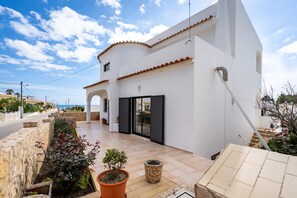 Ein weißes Gebäude mit einem Ziegeldach, einer überdachten Terrasse und Blick aufs Meer.
