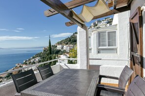 A terrace with a table and chairs, overlooking a coastal view with buildings and a clear sky.
