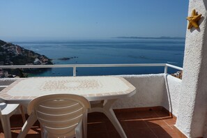 A balcony with a table and chairs, overlooking a coastal view with clear skies.