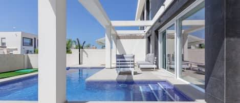 A modern pool area with a clear blue pool, white columns, and a seating area with a view of the pool.
