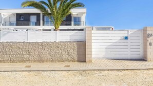 Un edificio moderno con un muro de piedra, una palmera y una entrada con portones.