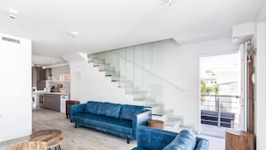 Un soggiorno moderno con un divano blu, un'area pranzo con un tavolo rotondo e una scala che conduce a un piano superiore.