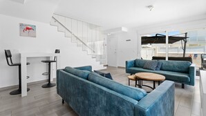 Een moderne woonkamer met een blauwe bank, een klein tafeltje en een trap.