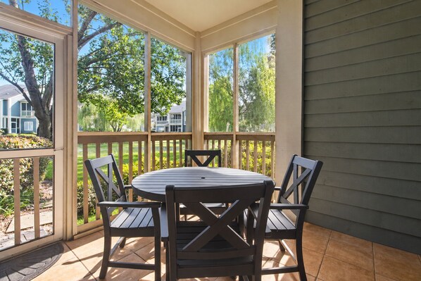 A covered patio with a round table and four chairs, surrounded by a wooden fence and large windows. - $150 activities - E-gift card when you book - 1st Floor with Screened in Porch | KC5D (Myrtle Beach)