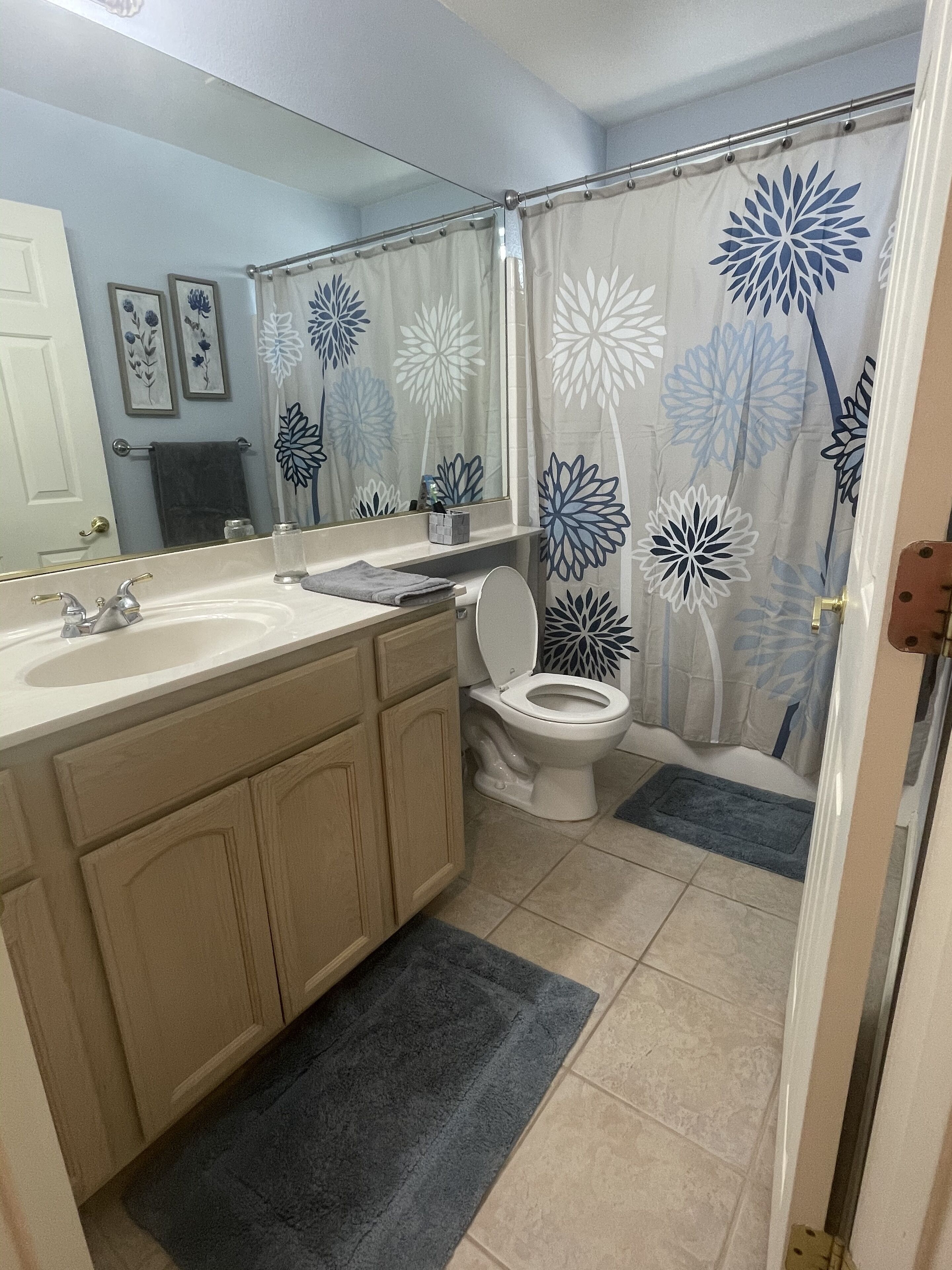 Baño con lavamanos doble, inodoro y cortina de ducha estampada con motivos florales.