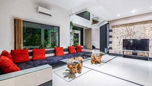 A modern living room with a glass coffee table, a sofa with red cushions, a flat-screen TV, and a decorative wall. - Anedda Mutiara Villa (Denpasar)