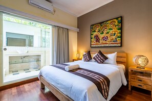 Un dormitorio bien iluminado con una cama grande, una mesita de noche con lámpara, un cuadro en la pared y una ventana con cortinas.