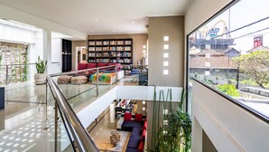 A modern multi-level living area with a glass railing, a large bookshelf, and a view of a roller coaster. - Anedda Mutiara Villa (Denpasar)