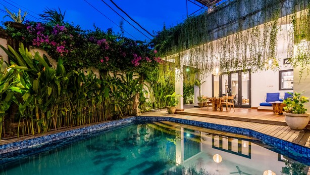 A swimming pool with tiled edges, surrounded by lush greenery and a patio area with outdoor furniture. - Anedda Mutiara Villa (Denpasar)