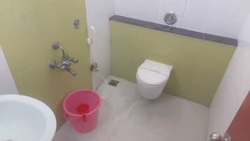 A small bathroom with a white sink, a pink bucket, a toilet, and a showerhead.