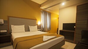 A hotel room with a large bed, a nightstand, a desk with a chair, a TV, and a wardrobe. - P K Rresidency (Madurai)