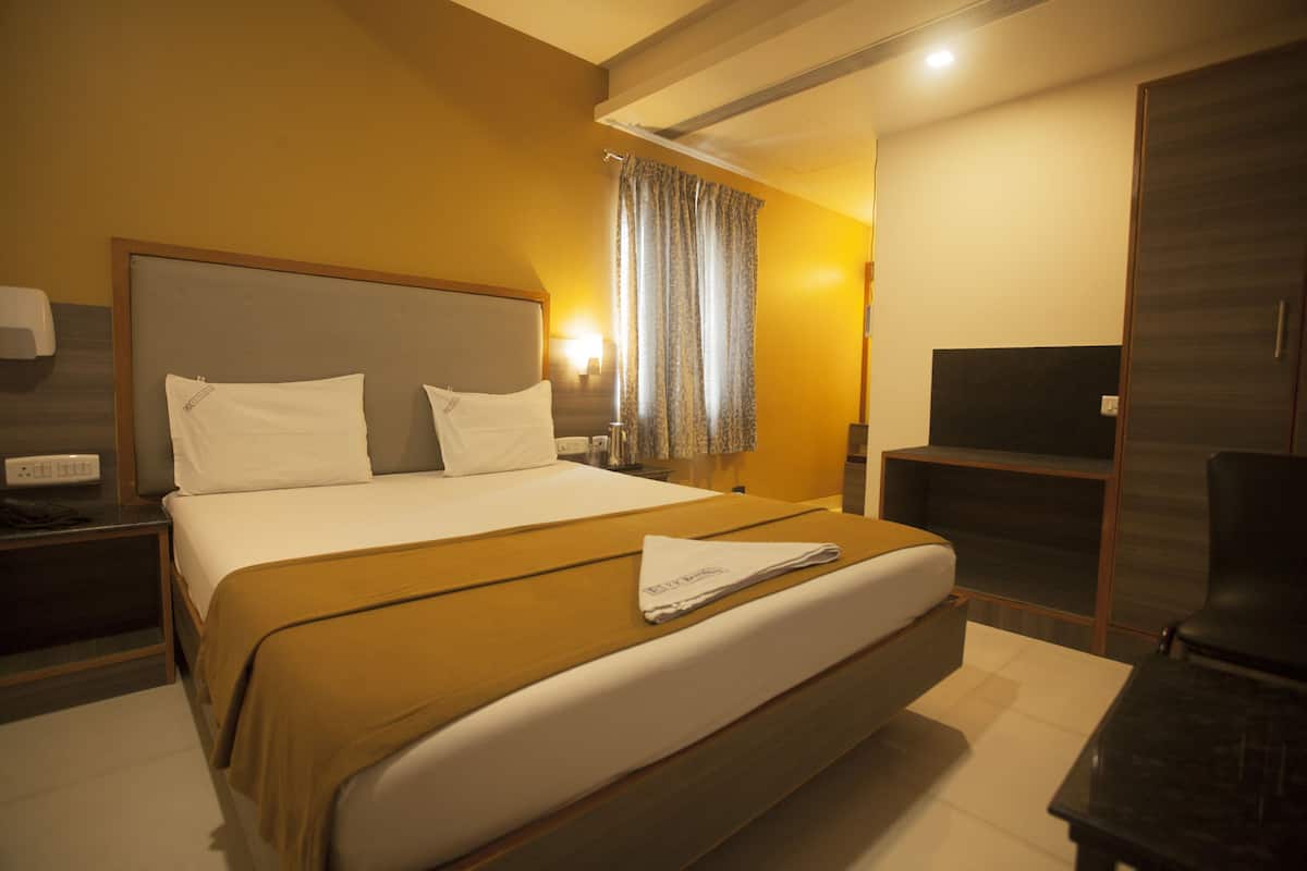 Quarto de hotel com uma cama grande, mesa de cabeceira, escrivaninha com cadeira, televisão e guarda-roupa.