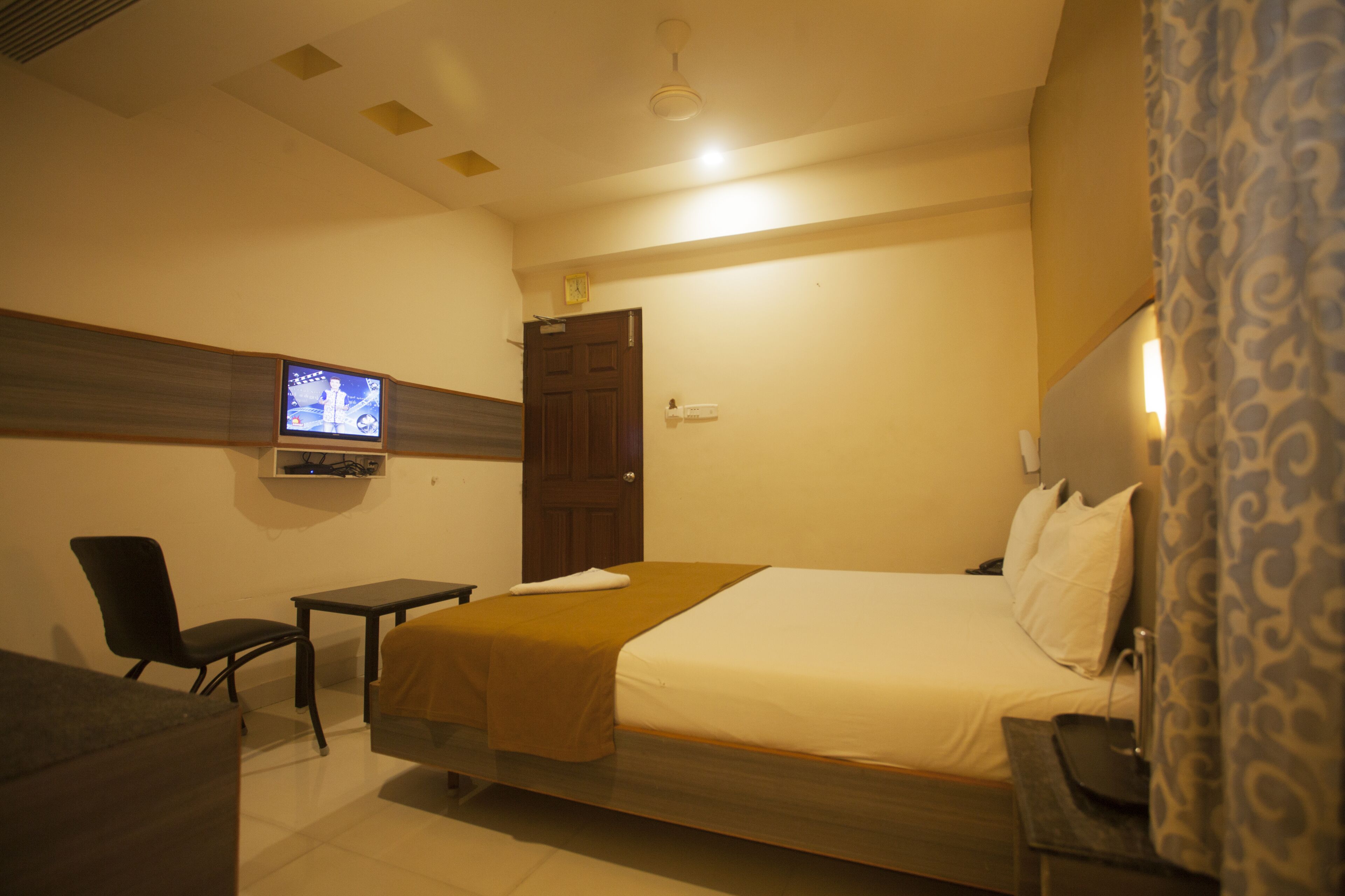 A hotel room with a bed, a desk, a chair, a television, and a door.
