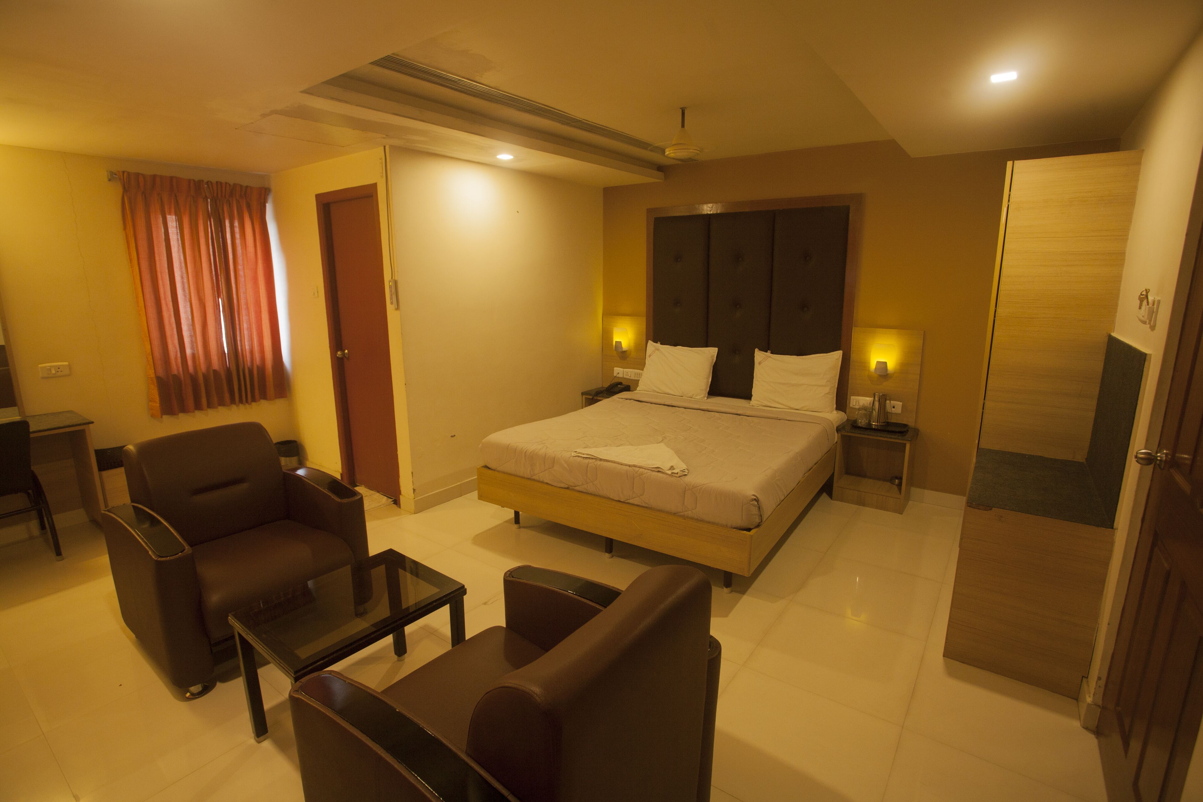 Quarto de hotel com cama, poltrona, mesa pequena, escrivaninha e guarda-roupa.